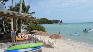 A beachside restaurant with outdoor seating, a view of the sea, and a few boats in the water. - JP Resort Koh Tao (Koh Tao)