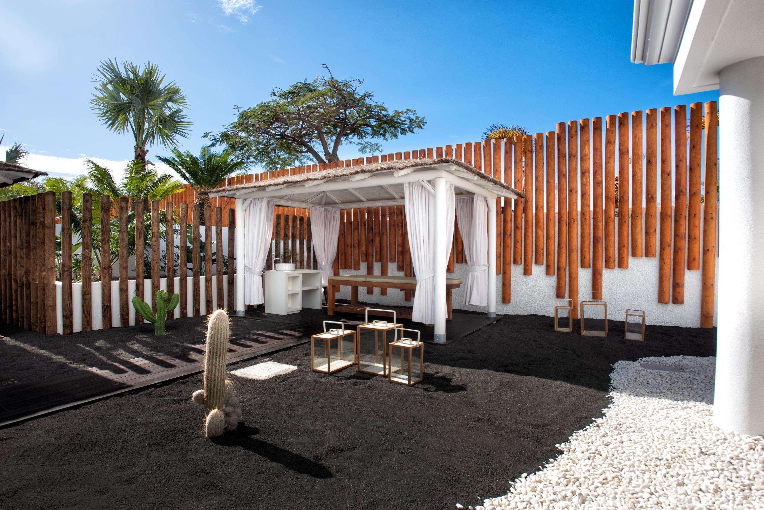 A patio area with a wooden fence, a covered seating area, and a cactus plant.