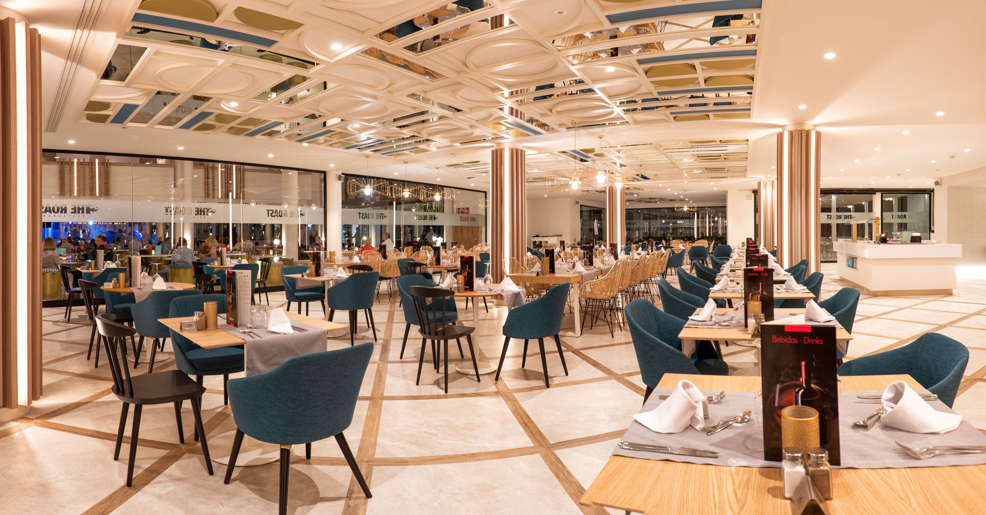 A spacious restaurant with a modern ceiling design, multiple dining areas, and a visible bar area.