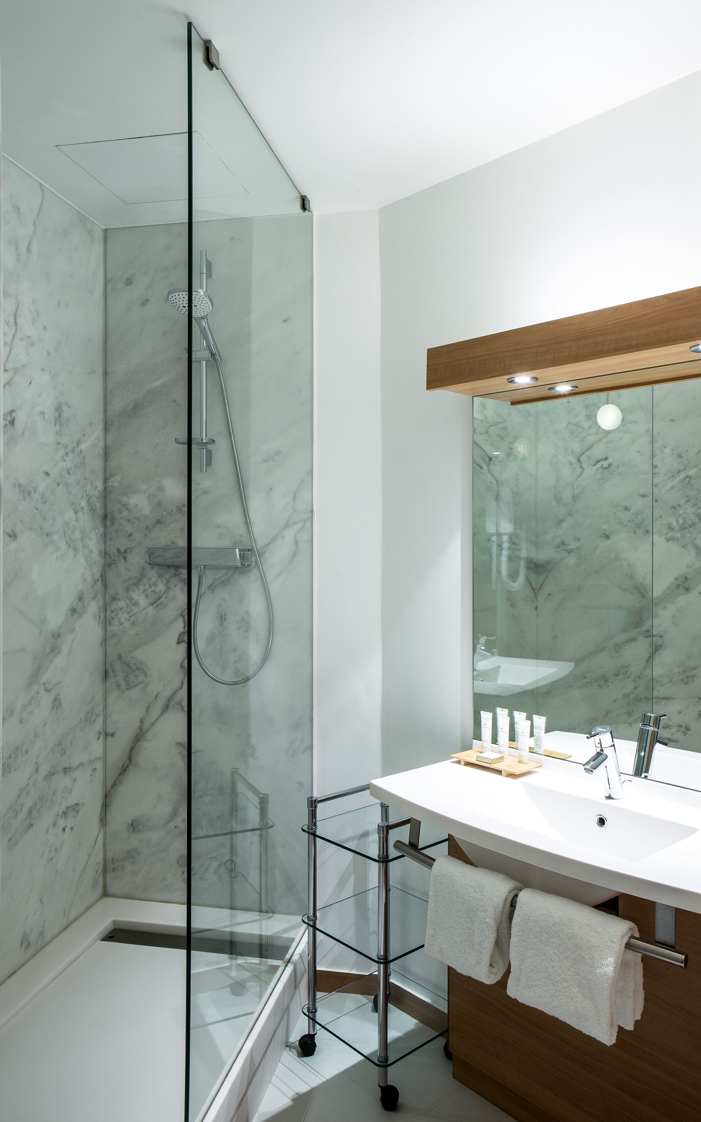 Un baño moderno con cabina de ducha de vidrio, un lavabo blanco con mueble de madera y un espejo grande.