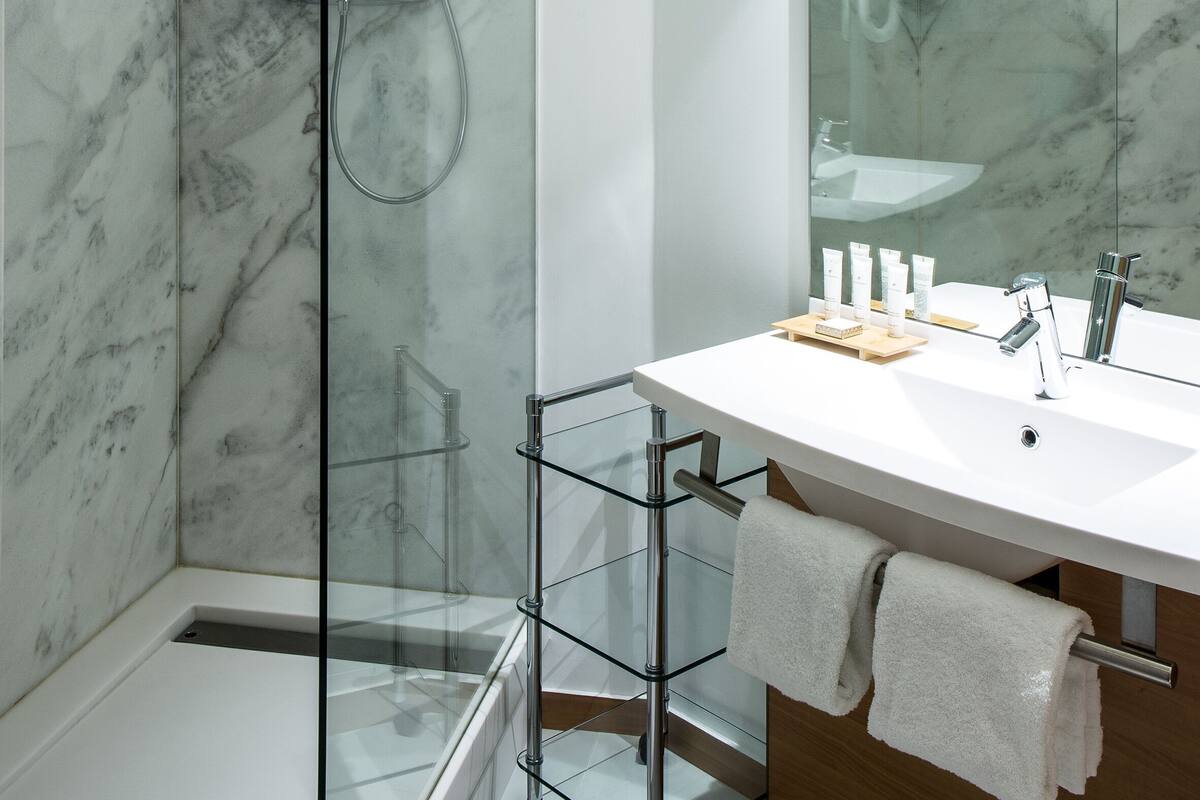 Ein modernes Badezimmer mit Duschkabine aus Glas, einem weißen Waschbecken mit Holzunterschrank und einem großen Spiegel.