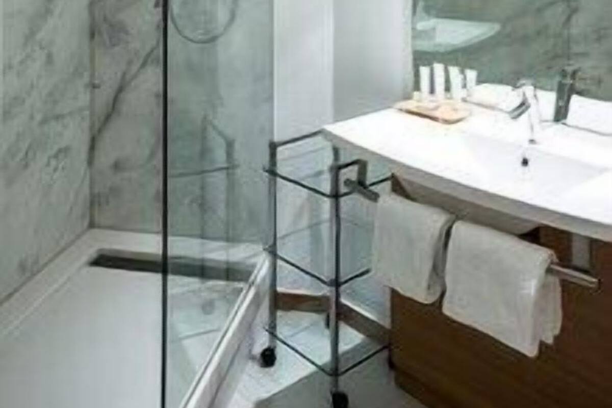 Ein Badezimmer mit Duschkabine aus Glas, einem weißen Waschbecken mit Holzschrank und einer Marmorwand.