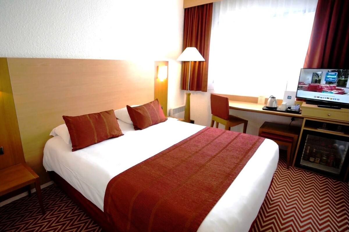 Ein Hotelzimmer mit einem großen Bett, einem Schreibtisch, einem Sessel und einem Fernseher.