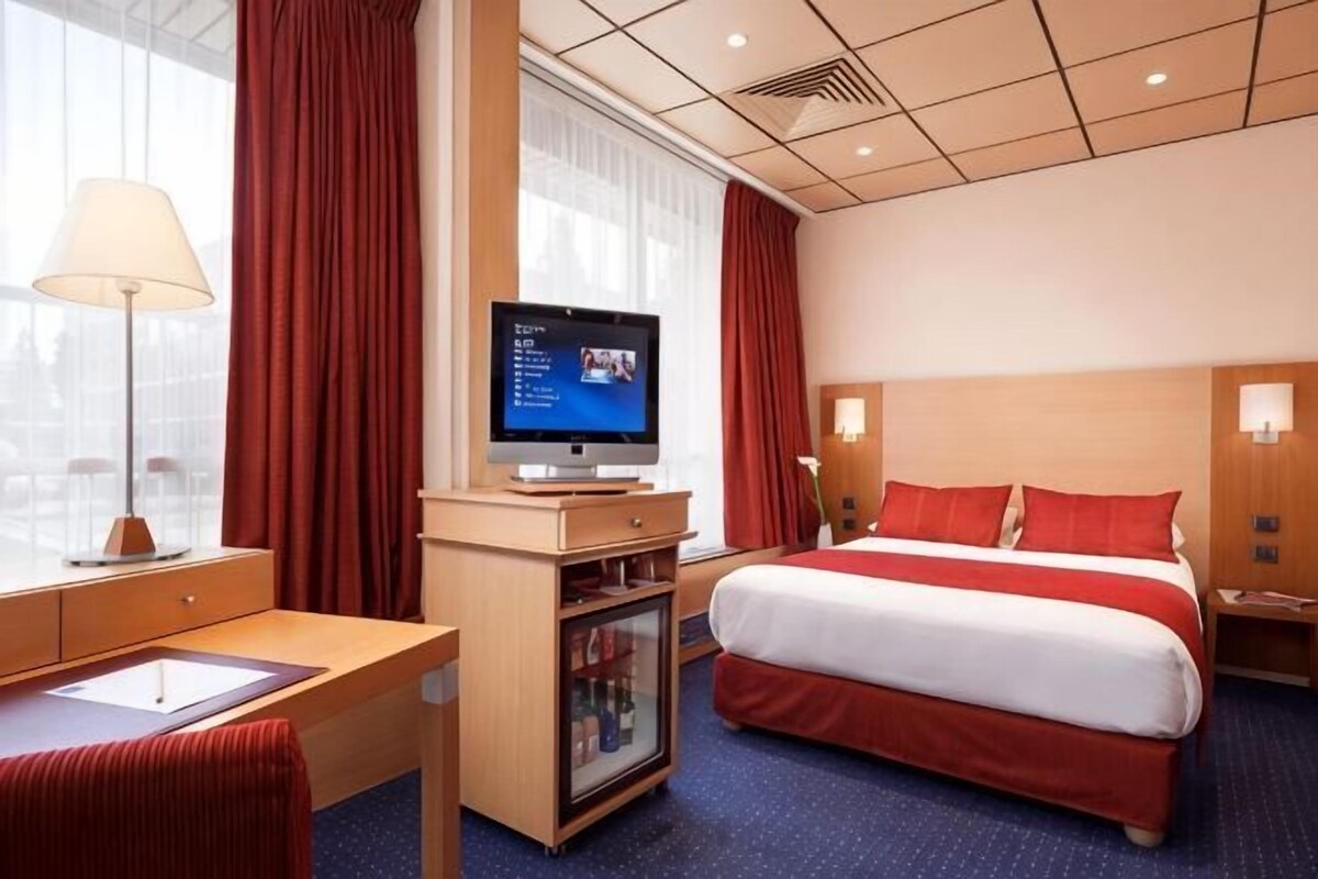 A hotel room with a bed, a desk, a television, and a window with curtains.