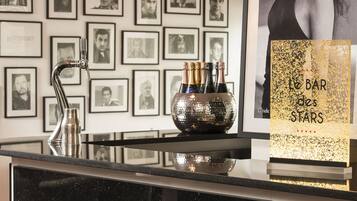 A bar area with a black countertop, two pendant lights, framed photographs on the wall, and a sign reading "Le Bar des Stars".