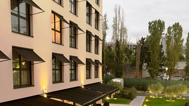 Een modern gebouw met een overdekte terras en een verzorgd gazon, met een rij ramen.