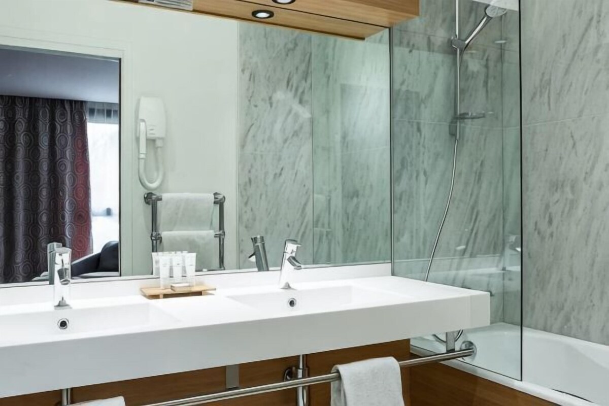 A modern bathroom with a large mirror, two sinks, a shower, and a bathtub.