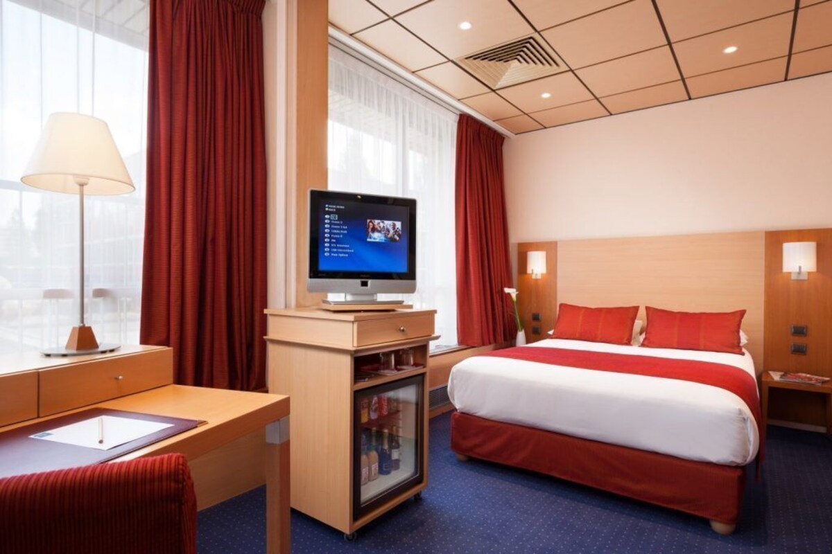 A hotel room with a bed, desk, television, and a minibar.