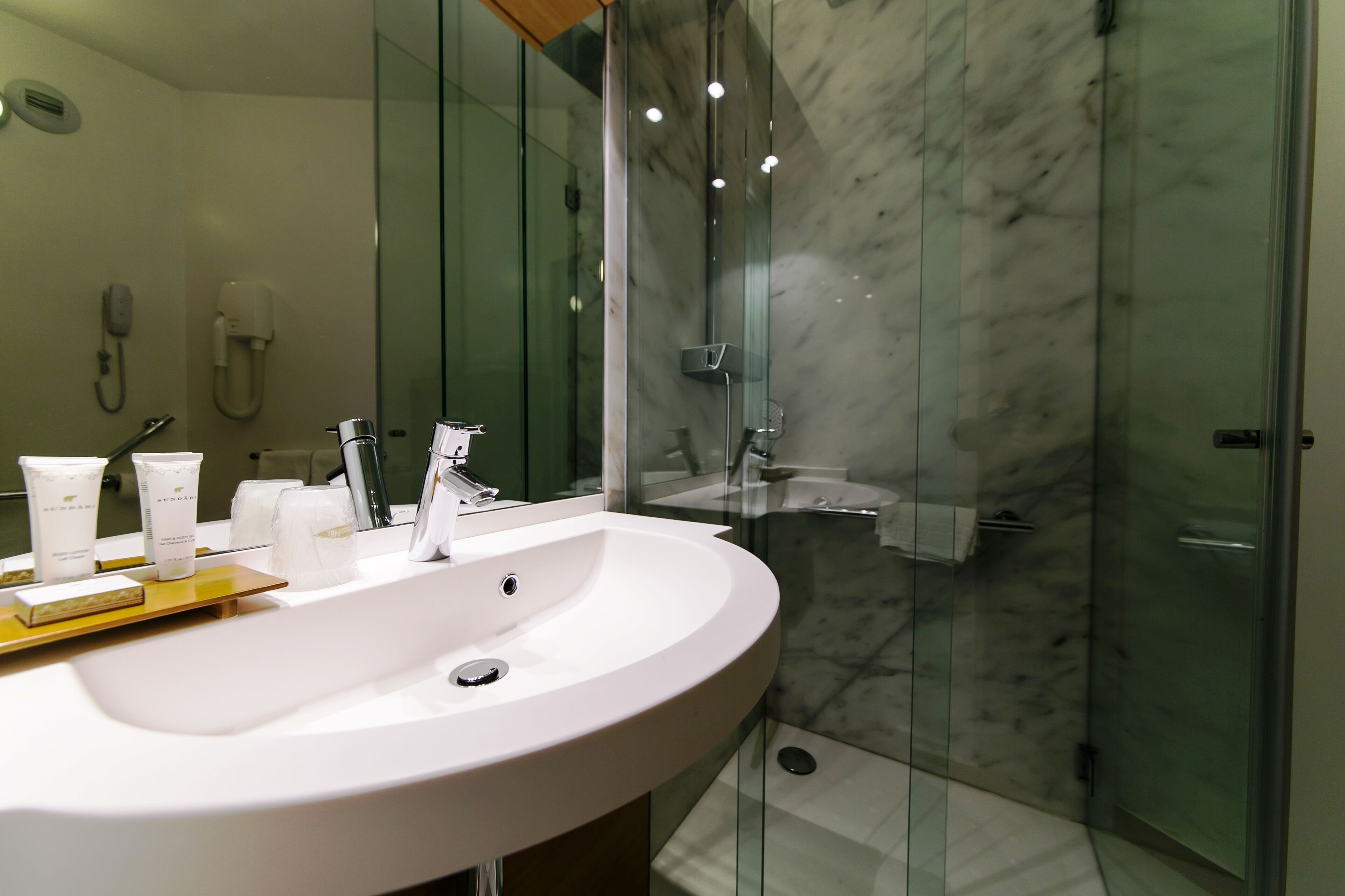 A modern bathroom with a white sink, glass shower enclosure, and marble walls.