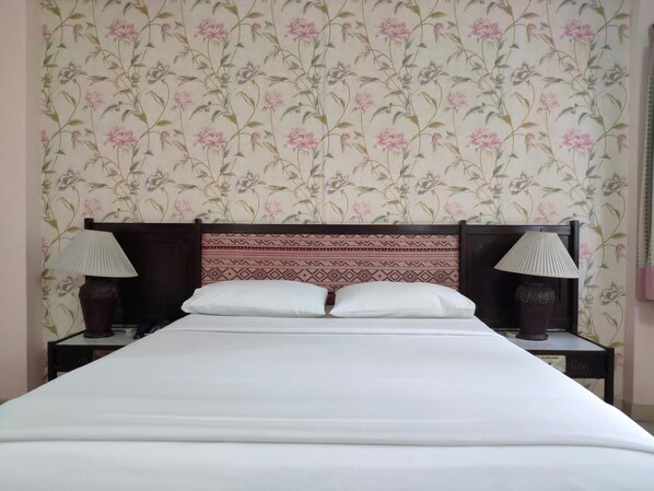 Una cama con cabecera de madera, dos lámparas de noche y un estampado de flores en el papel tapiz.
