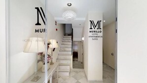 Ein Hotel Eingang mit einer Treppe, einer Chandelüster und Schildern mit der Aufschrift 'MURILLO HOTEL APARTMENTS SUITES'.