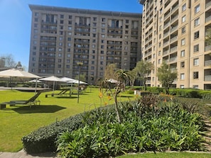 Un edificio residencial de gran altura con varios balcones, un césped bien cuidado y zonas de estar al aire libre.
