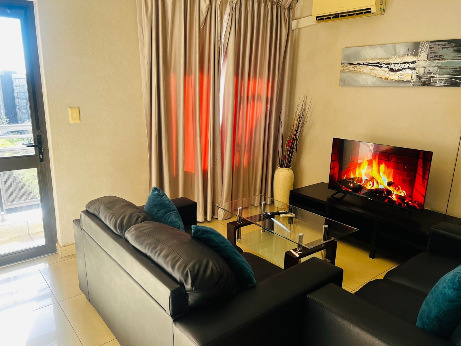 A modern living room with a leather sofa, a glass coffee table, and a flat-screen TV displaying a fireplace.