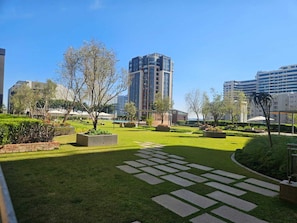 A landscaped courtyard with a central pathway, surrounded by greenery and modern buildings in the background.