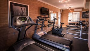 Un gimnasio con cintas de correr, una elíptica, una bicicleta estática y un estante con mancuernas.