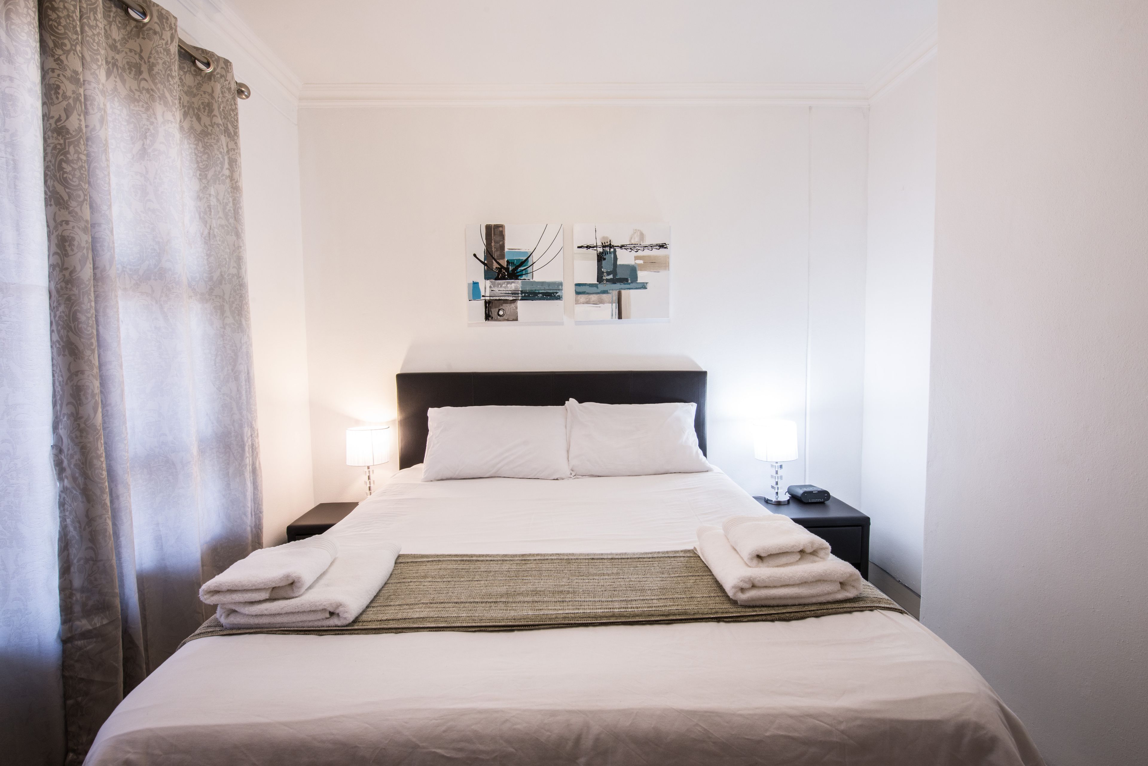 A neatly made bed with white linens, a bedside table with a lamp, and a wall art piece above the bed.