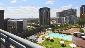 Un edificio de gran altura con piscina en la azotea, rodeado de otros edificios y vegetación.