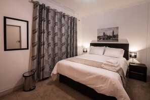 Ein ordentlich eingerichtetes Hotelzimmer mit einem Bett, einer Nachttischlampe, einem gerahmten Bild an der Wand und einem Papierkorb.