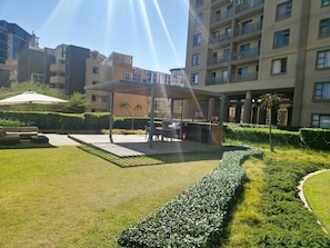 A courtyard with a covered seating area, a pathway, and well-maintained hedges.