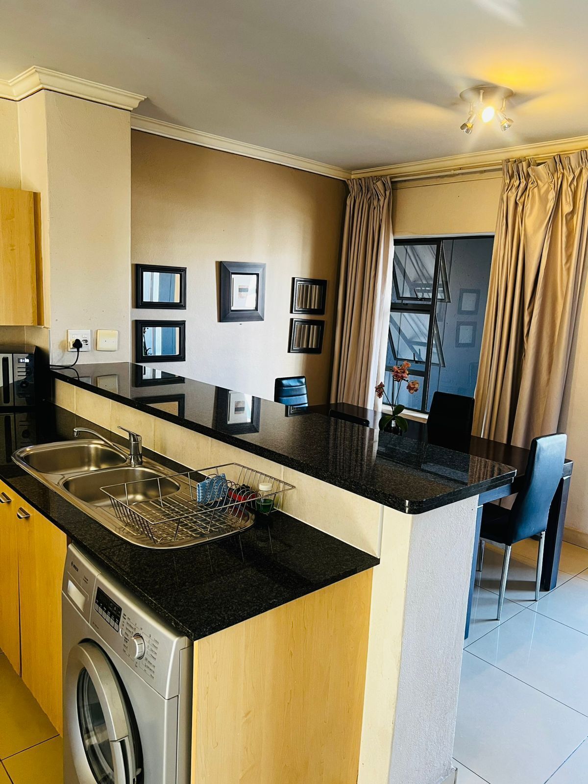 Una cocina compacta con lavadora integrada, un comedor con mesa y sillas, y una ventana con cortinas.