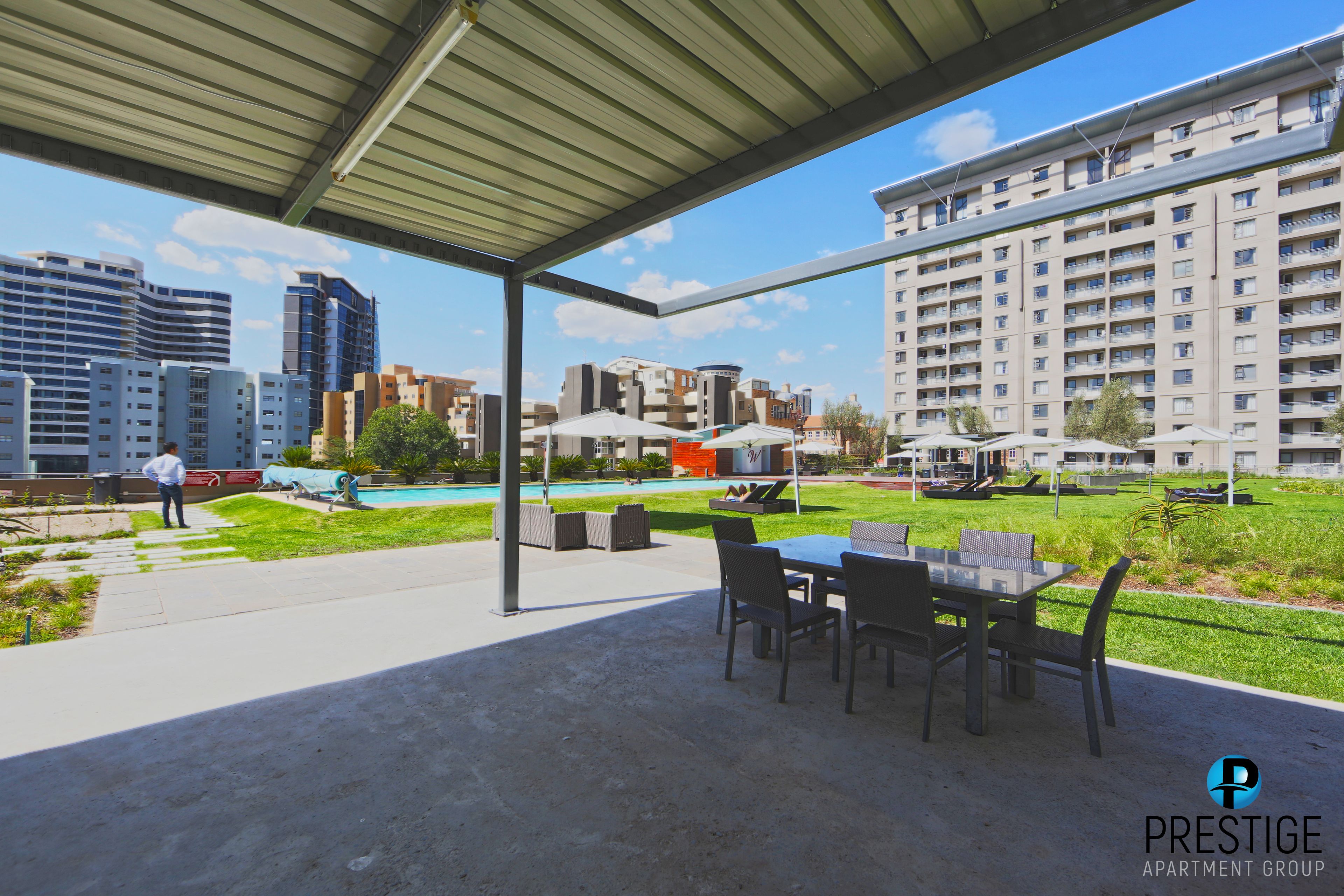 An outdoor patio area with a covered seating area, a pool, and a view of surrounding buildings.