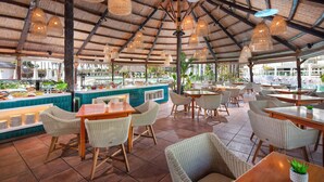 Un restaurante con mobiliario de mimbre, un bufé y una piscina al fondo.