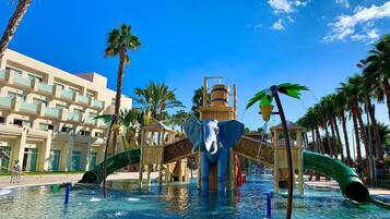 Un parco acquatico con una grande statua di elefante, palme e un albergo sullo sfondo.