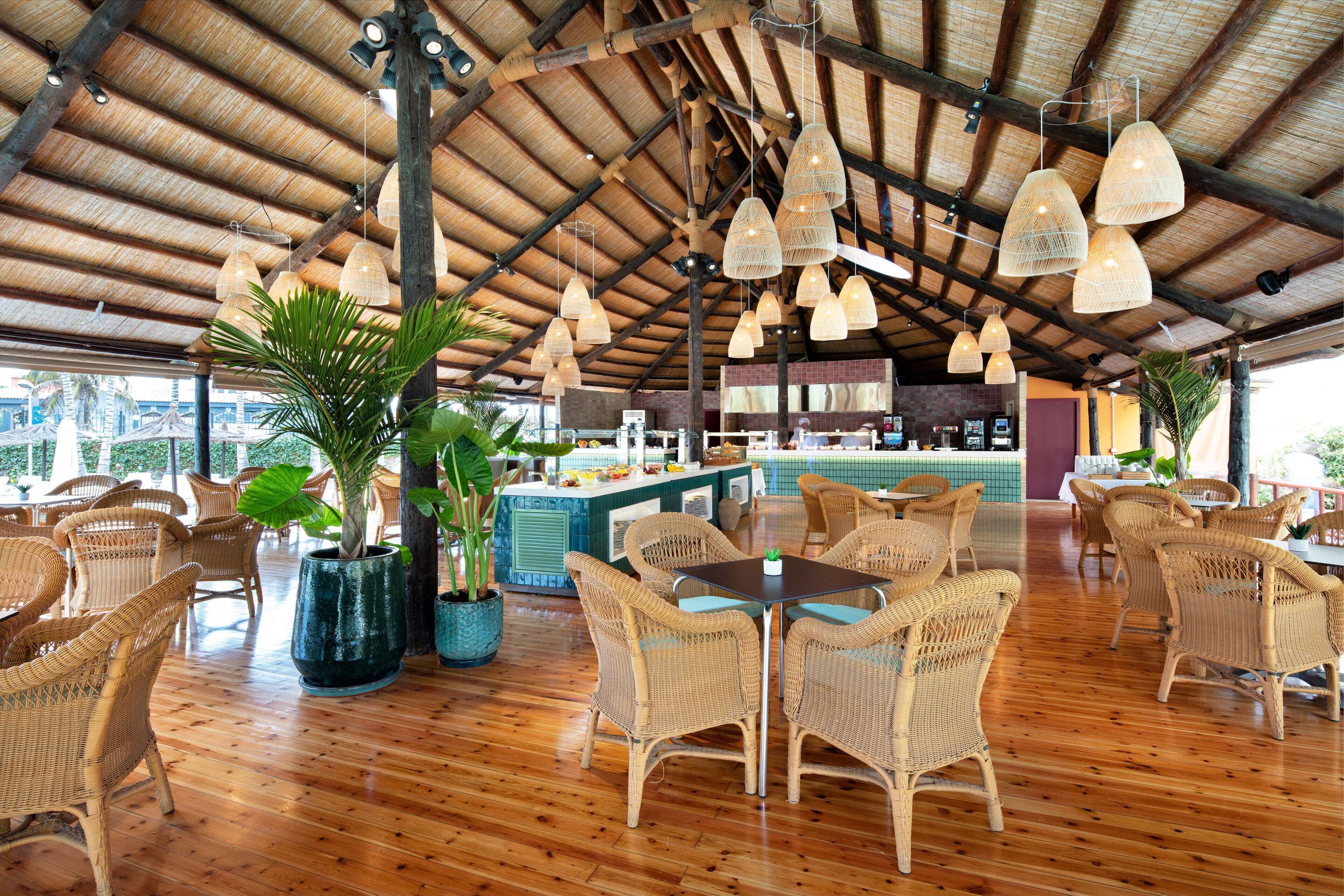 A spacious indoor area with wooden flooring, wicker furniture, and hanging light fixtures.
