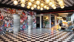 A lobby with a checkered floor, graffiti walls, and a seating area with a check-in desk. - Moxy Paris La Villette (Paris)