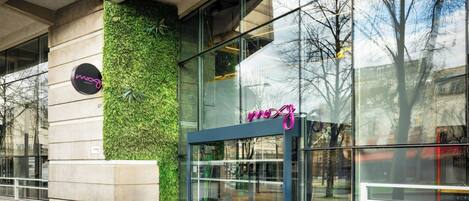 A modern building with a glass facade, a neon sign, and a green vertical garden.