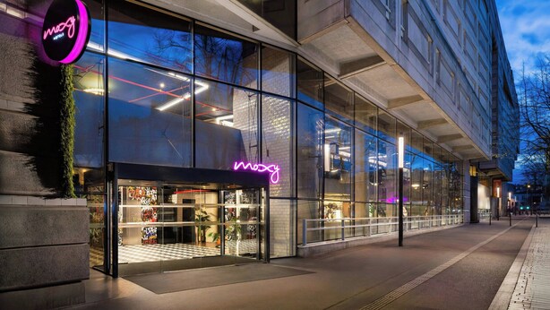 A modern building with large glass windows and a neon sign. - Moxy Paris La Villette (Paris)