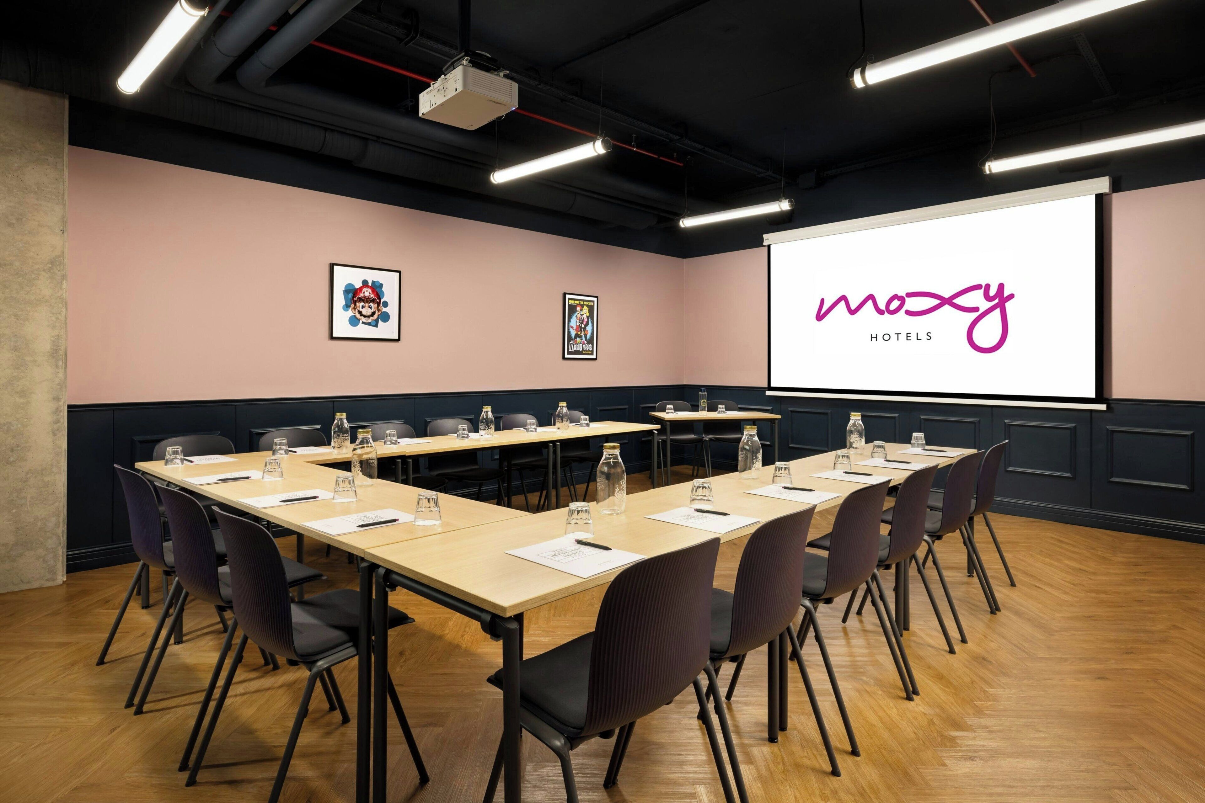 A conference room with a long table, chairs, a projector screen, and framed artwork on the wall.