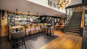 A bar area with stools, a counter, and a staircase leading to an upper level. - Moxy Paris La Villette (Paris)