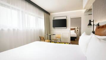 A hotel room with a bed, a TV mounted on the wall, a small round table with two chairs, and a mirror.