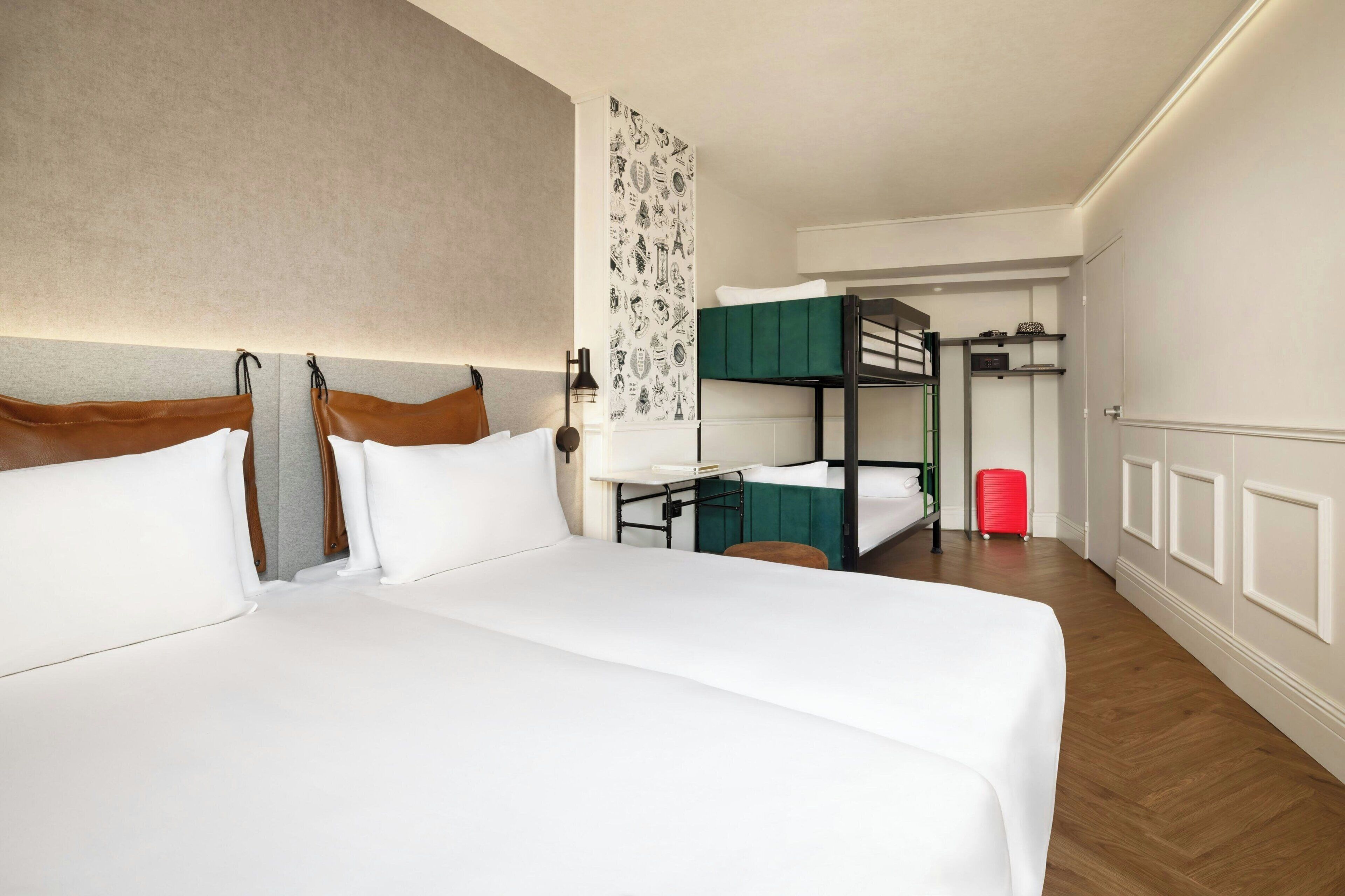 A hotel room with a large bed, a desk, a bunk bed, and a patterned wall.