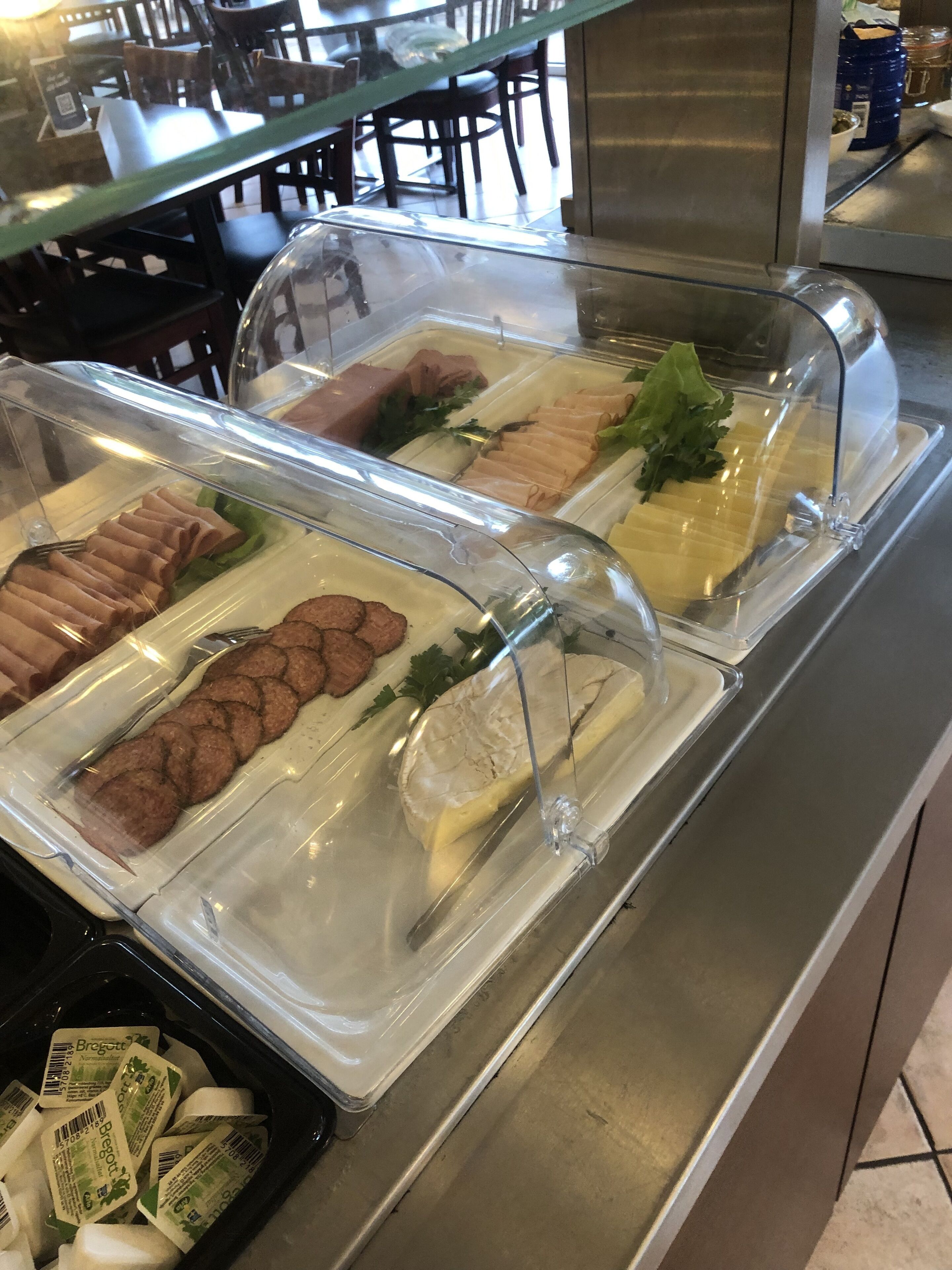 Un bufé con distintos alimentos, como carnes y quesos, expuestos en recipientes de plástico transparente.