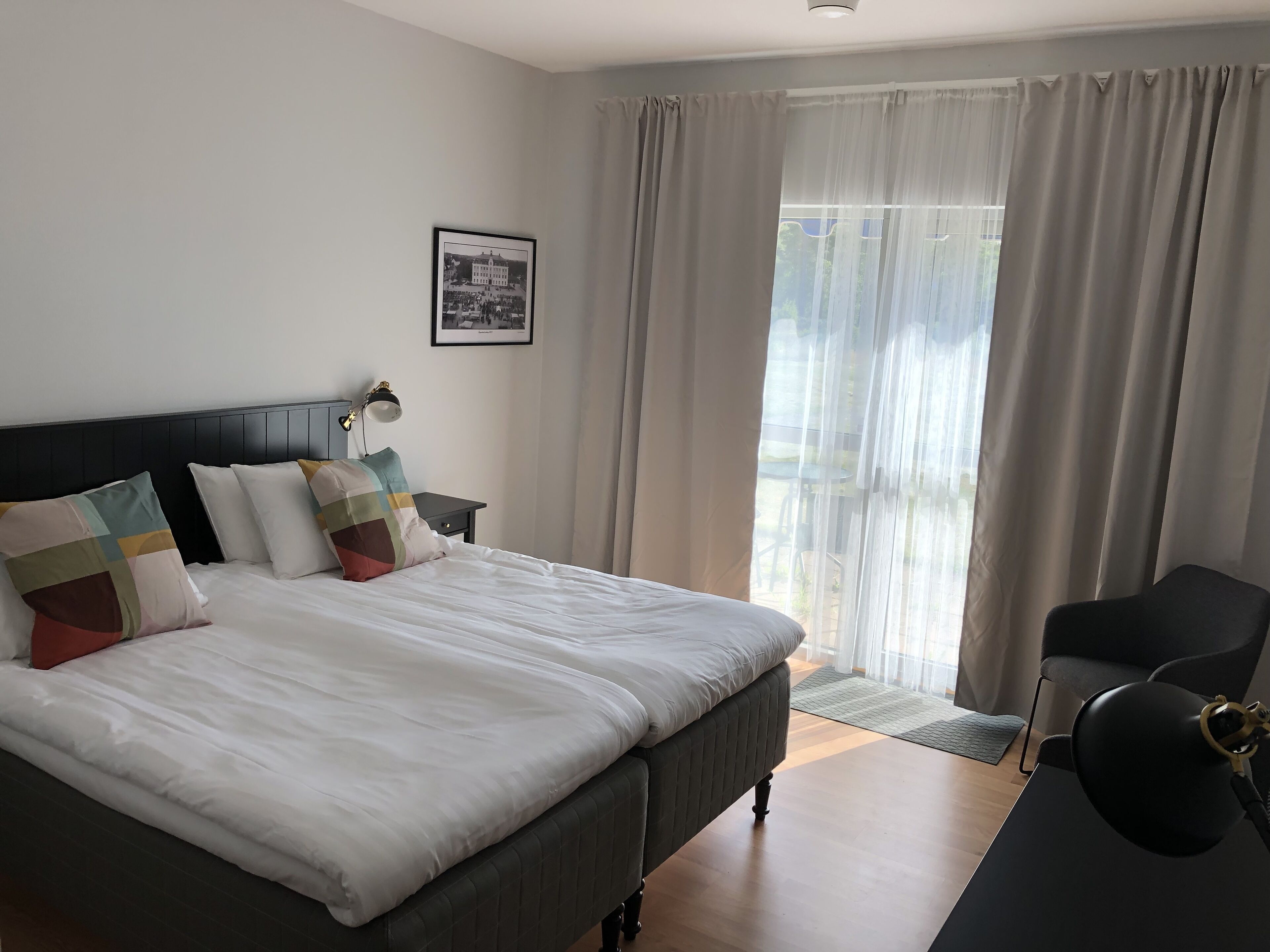Una habitación de hotel moderna con una cama grande, un escritorio, una silla y un ventanal con cortinas.