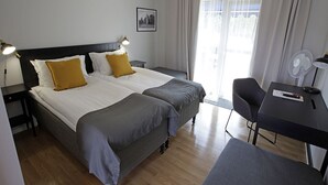 A hotel room with two beds, a desk, a chair, and a window with curtains.
