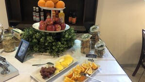 A buffet table with various food items including apples, oranges, grapes, and sliced bananas.