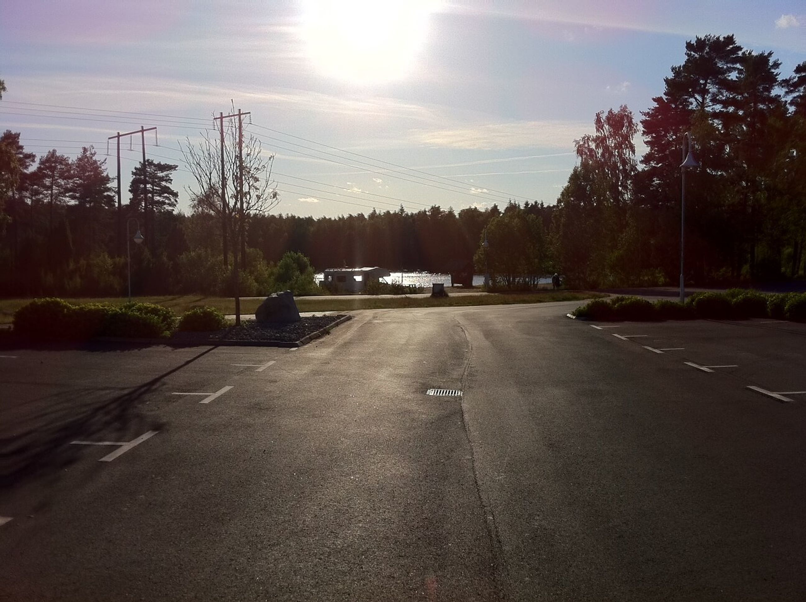 En parkeringsplats med markerade parkeringsrutor, en byggnad i bakgrunden och träd runt omkring.