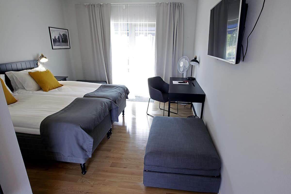 A hotel room with two beds, a desk, a chair, a TV, and a window with curtains.