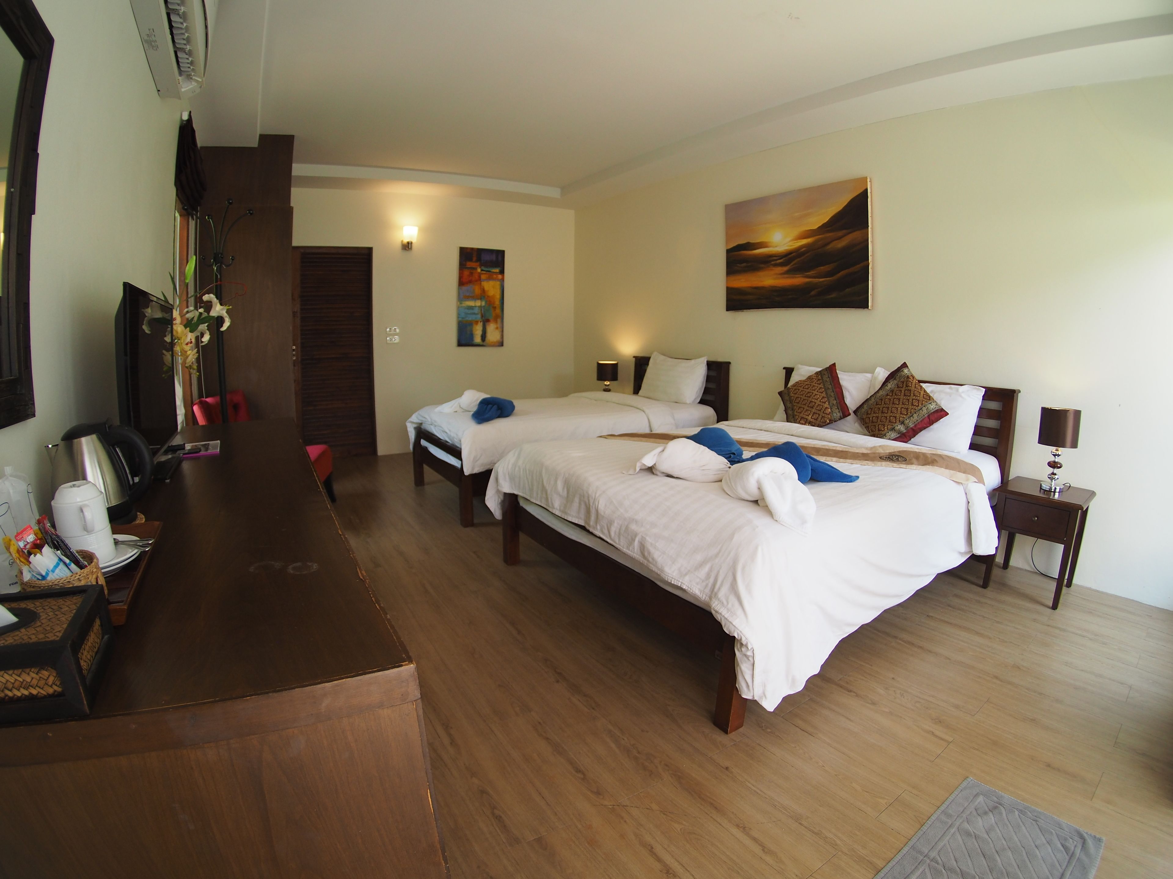 A hotel room with two beds, a wooden desk, a coffee maker, and a painting on the wall.