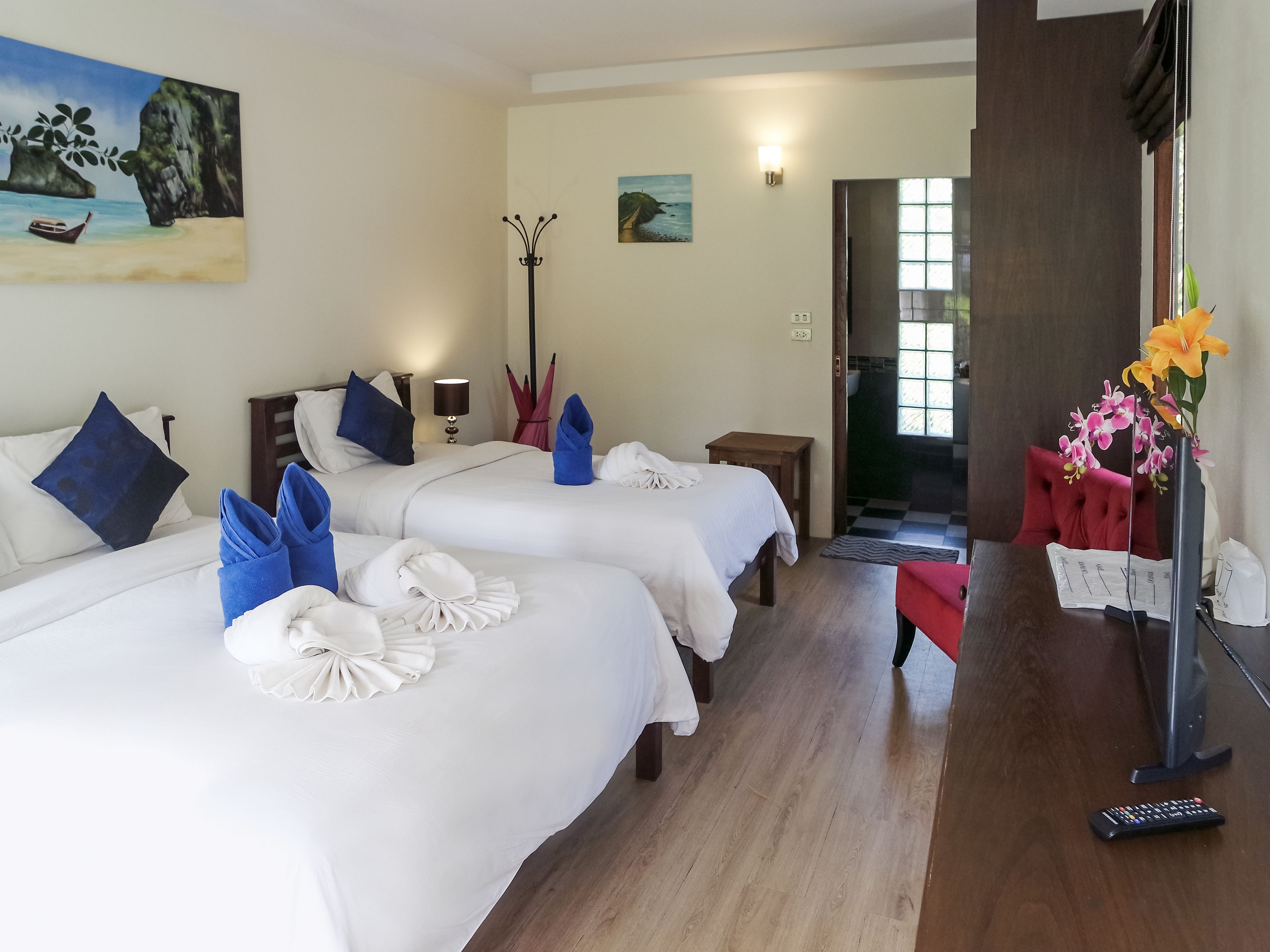 A hotel room with two beds, a desk, a chair, a lamp, and a painting on the wall.