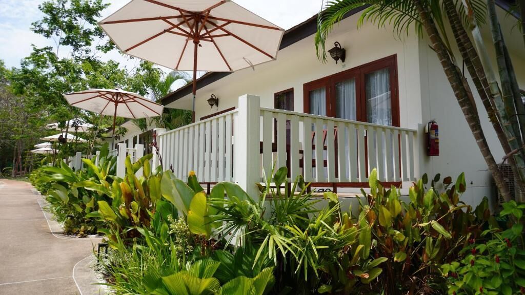 A white building with a white fence, outdoor umbrellas, and tropical plants.