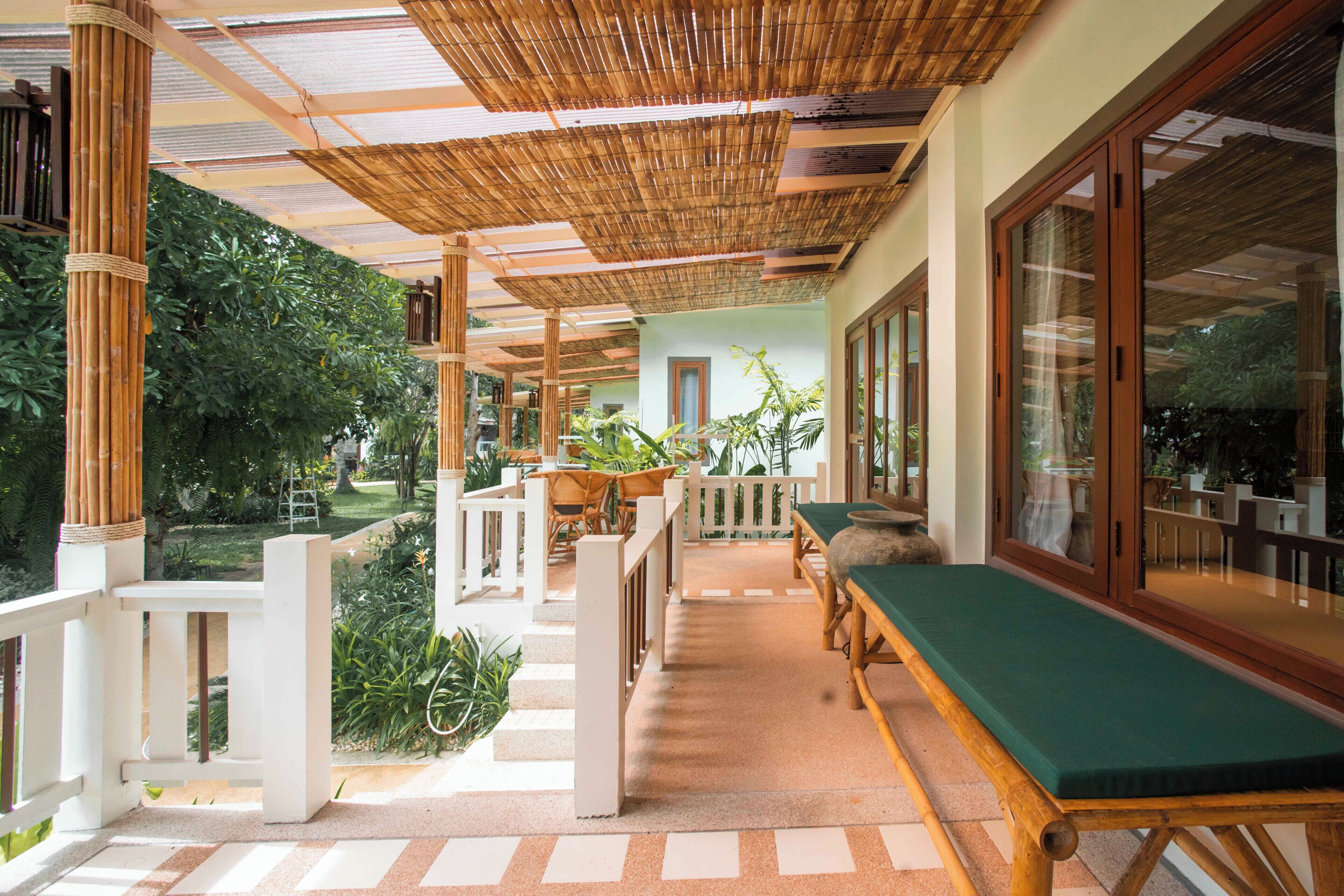 A covered outdoor area with a wooden bench, potted plants, and a view of the surrounding garden.