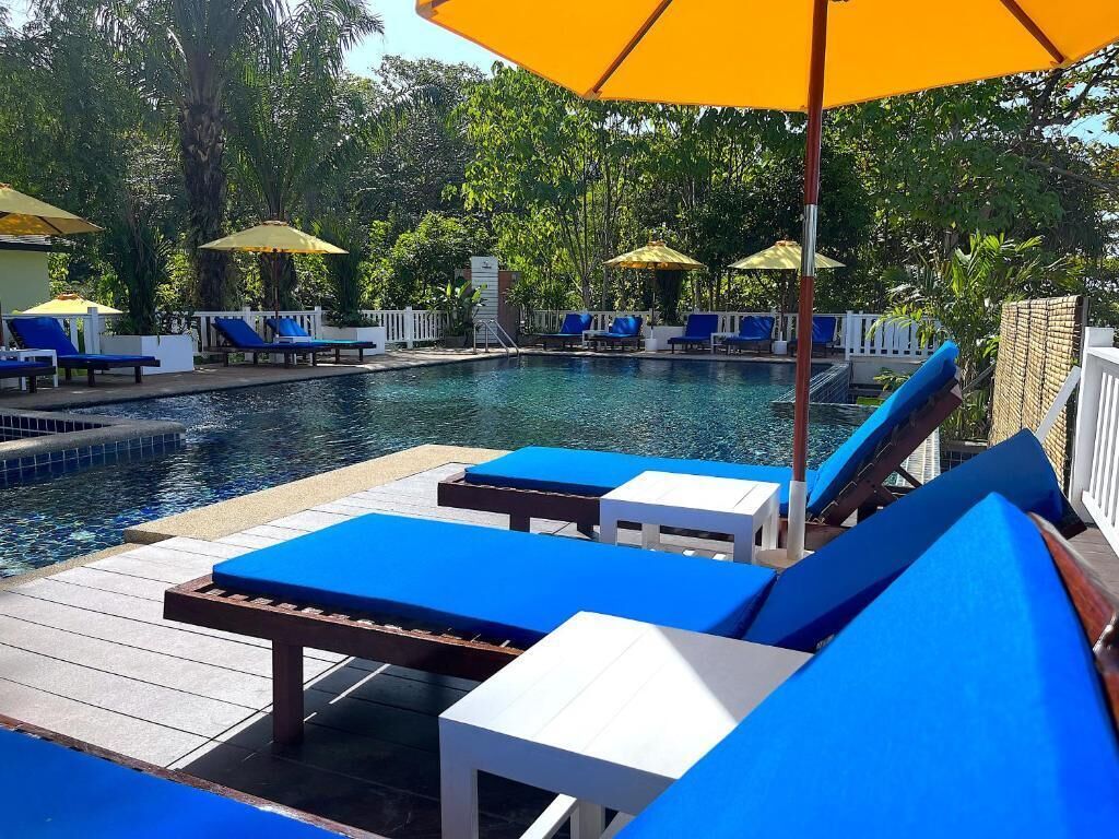Un área junto a la piscina con sillas reclinables azules y sombrillas amarillas.