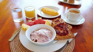 Un desayuno con tostadas, un tazón de yogur, una rebanada de sandía y dos vasos de jugo de naranja.