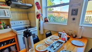 Een keuken met een houten tafel, een waterkoker, een mok, borden, en een schaal met eten.