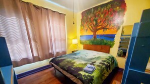 Een slaapkamer met een bed, gordijnen, een schilderij van een boom, een lamp en een houten vloer.