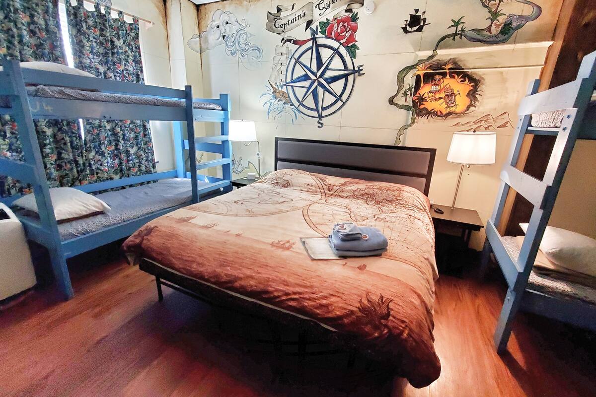 Um quarto com beliches, uma cama com colcha estampada e um mural na parede com motivos náuticos.